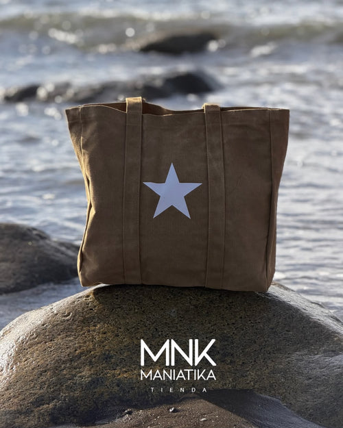 Bolso Estrella en color café, con la estrella blanca al frente, apoyado sobre una roca con el mar de Matanzas detrás.